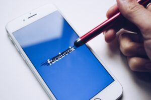 smartphone with facebook loading page and person scratching out facebook logo with stylus