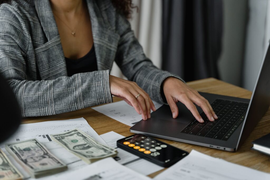 a woman in a plaid blazer using her laptop with US dollars cash